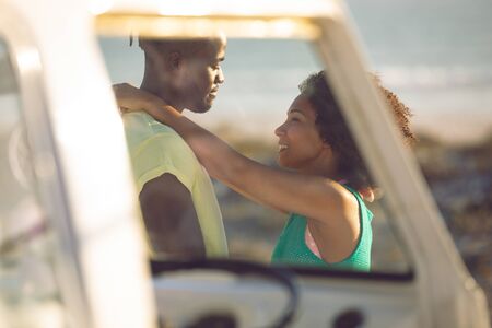 Side view of romantic mixed race couple embracing each other near camper van at beachの写真素材