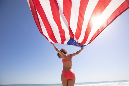 Low angle view of African american woman in bikini holding american flag on the beach