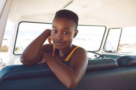 Front view of happy African american woman looking at camera while sitting in a camper van at beach
