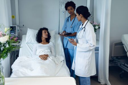 Side view of diverse female doctors interacting with mixed race female patient in the ward at...
