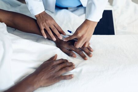 Close up on mixed race female doctor attaching iv drip on African-American male patient hand in the ward at hospitalの写真素材