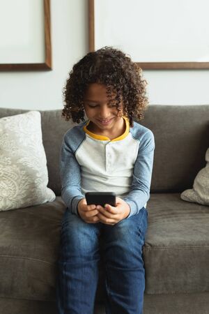 Front view of happy mixed race boy using mobile phone in the lobby at hospital
