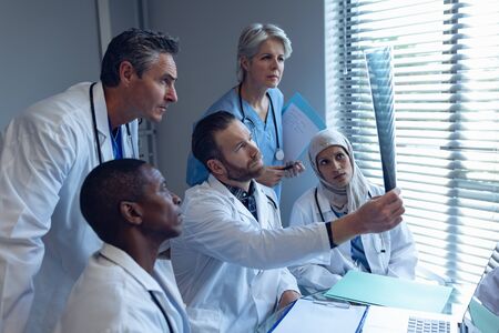 Side view of attentive medical diverse team looking at x-ray at desk in hospital
