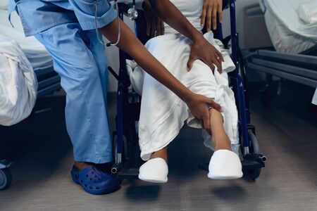 Low section of African-American female doctor helping disabled female patient to move her legs in the ward at hospitalの写真素材