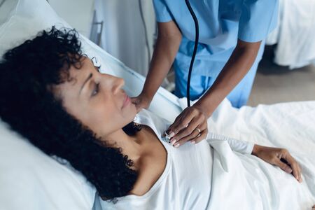 Side view of African-American female doctor examining female patient with stethoscope in the ward at hospitalの写真素材