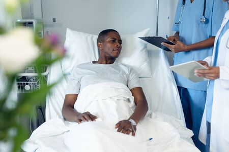 Side view of diverse female doctors interacting with African-American male patient in the ward at...