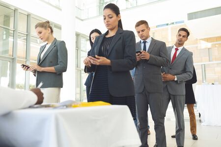 Front view of group of diverse business people queuing up for interview while texting on mobile...