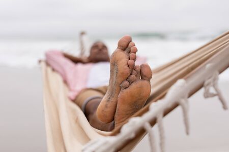 Low angle view of African American Man sleeping with hands behind head on a hammock at beachの写真素材
