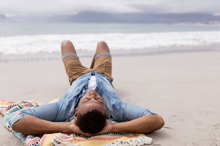 Rear view of African american Man sleeping with hands behind head at beach on a sunny dayの写真素材