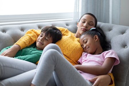 Front view of African american Mother and children sleeping together on a sofa in living room at...
