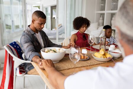Over the shoulder view of happy mixed-race multi-generation family praying before having meal on...