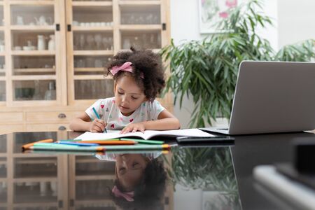 Front view of African american cute girl doing her homework on a table at home