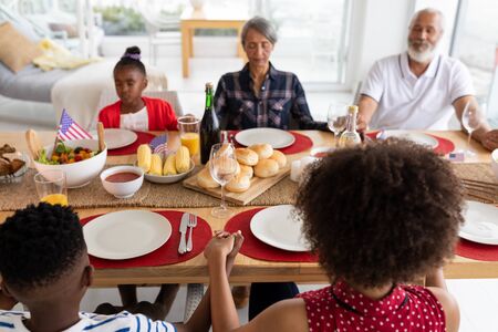 Over the shoulder view of happy mixed-race multi-generation family praying before having meal on...