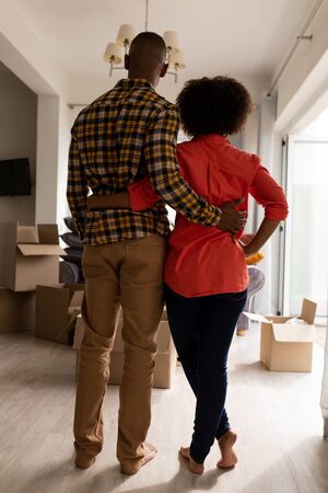 Rear view of African american couple standing together with arm around in living room at homeの写真素材