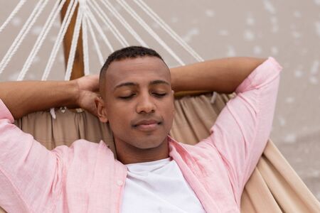 Front view of African American Man sleeping with hands behind head on a hammock at beach
