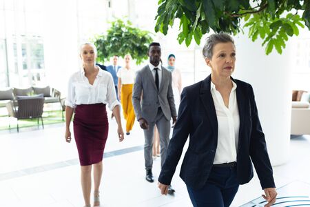 Front view of diverse business people walking straight ahead in modern office