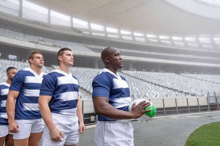 Side view of diverse male rugby player standing in a row at the entrance of stadium for matchの写真素材