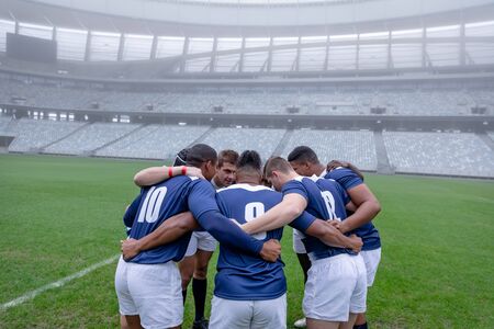 Side view of group of male rugby players forming huddles in the morning at stadiumの写真素材