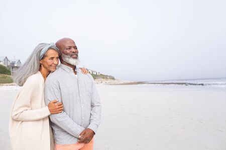 Front view of happy senior African-American couple standing on the beach on cloudy day. Authentic...