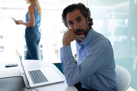 Front view of Caucasian businessman with hand on chin looking at camera while businesswoman standing...