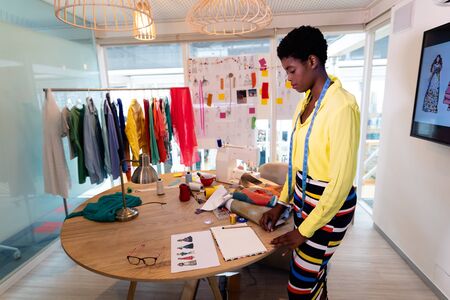Front view of pretty young African american female graphic designer looking at sketch in design...
