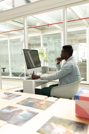 Side view of African american male graphic designer using graphic tablet at desk in office. This is...