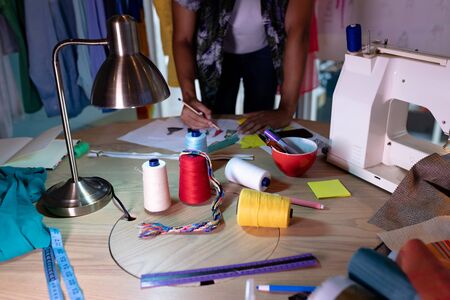 Mid section of young mixed race male fashion designer drawing a sketch at desk in design studio. This is a casual creative start-up business office for a diverse teamの写真素材