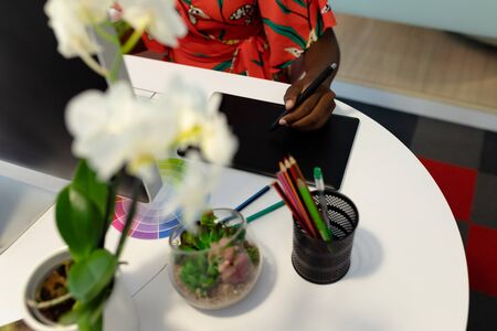 Mid section of African american female graphic designer using graphic tablet at desk. This is a...