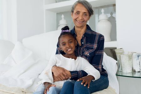 Portrait close up of African-American girl and mixed race grandmother sitting on bed. Authentic...