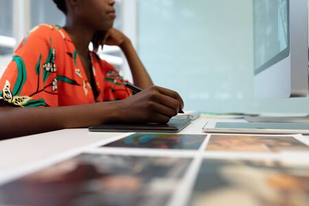 Mid section of African american female graphic designer working on graphic tablet at desk in office....