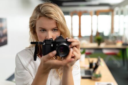 Front view of beautiful Caucasian female graphic designer clicking pictures with digital camera in...