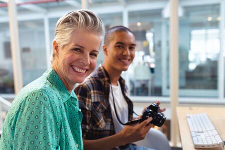 Portrait of diverse male and female graphic designers sitting together at desk in office. This is a casual creative start-up business office for a diverse teamの写真素材