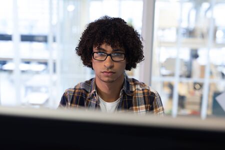 Front view of mixed-race male graphic designer working on computer at desk in office. This is a...