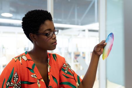 Side view of young African american female graphic designer looking at color swatch in office. This...