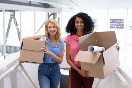 Portrait of young diverse female executives standing with cardboard boxes in office. This is a...