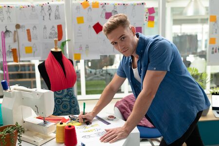 Portrait of Caucasian male fashion designer drawing sketch on a table in design studio. This is a casual creative start-up business office for a diverse teamの写真素材