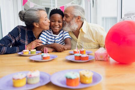 Front view of senior African-American man and woman kissing their grandson for his birthday party....