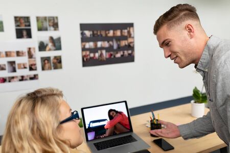 Rear view of Caucasian graphic designers discussing over laptop at desk in office. This is a casual...