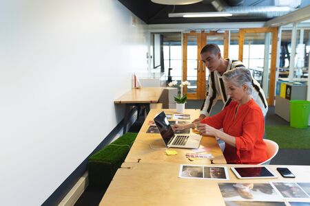 Side view of diverse graphic designers working together at desk in office. This is a casual creative...