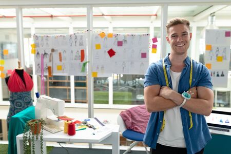 Portrait of Caucasian male fashion designer standing with arms crossed in design studio. This is a...