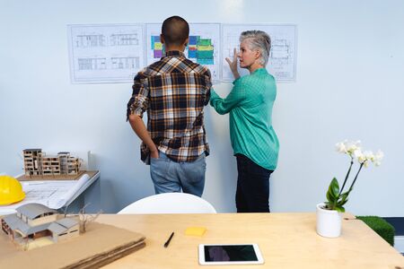 Rear view of diverse male and female architects discussing over an architectural plan in office....