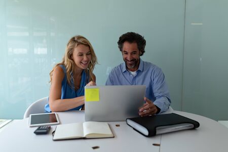 Front view of happy Caucasian business people discussing over laptop at desk in a modern office....