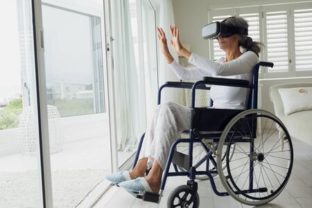 Side view of woman on wheelchair using virtual reality mask indoor. Authentic Senior Retired Life Conceptの写真素材