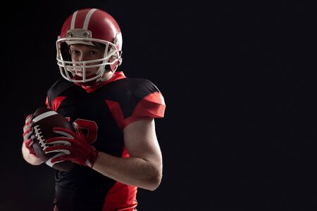 Young American football player in helmet standing against black background. Strong American Football Player concept for Championship Football Tournamentの写真素材