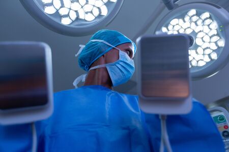 Low angle view of Mixed-race female surgeon using defibrillator while looking away  in operating...