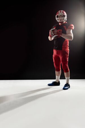 American football player in helmet holding rugby ball. Strong American Football Player concept for Championship Football Tournamentの写真素材
