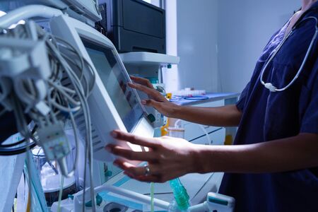 Mid section of young African-american female surgeon using medical equipment in operating room at...