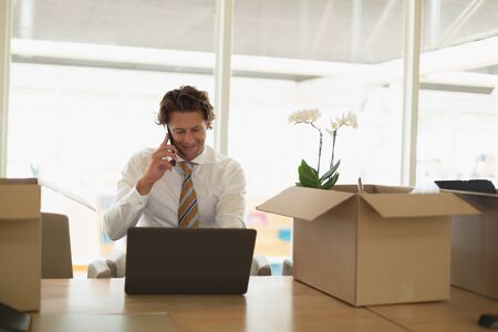 Front view of handsome young Caucasian businessman talking on mobile phone while using laptop in the conference room at office. New start-up business with entrepreneur working hardの写真素材