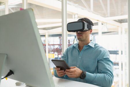 Front view of handsome young Caucasian male executive holding digital tablet while using virtual...
