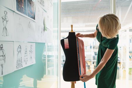 Side view of beautiful mature Caucasian female fashion designer using measuring tape on a mannequin in design studio. Modern casual creative business conceptの写真素材